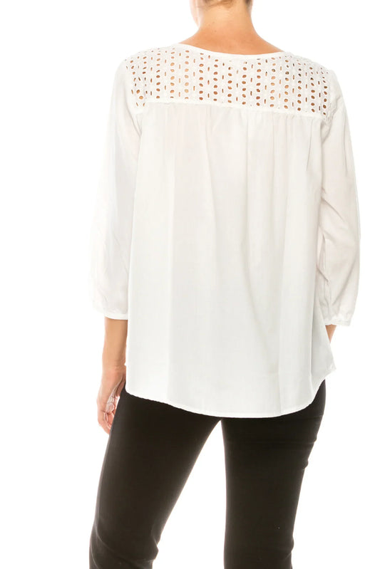 Back view of a woman wearing a white long-sleeve blouse with eyelet embroidery and black pants
