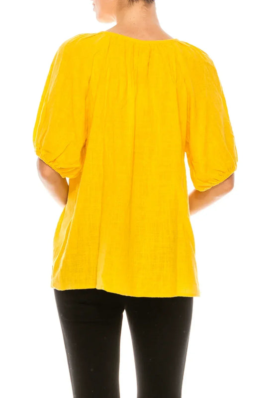 Back view of a woman wearing a bright yellow puff-sleeve blouse and black pants.