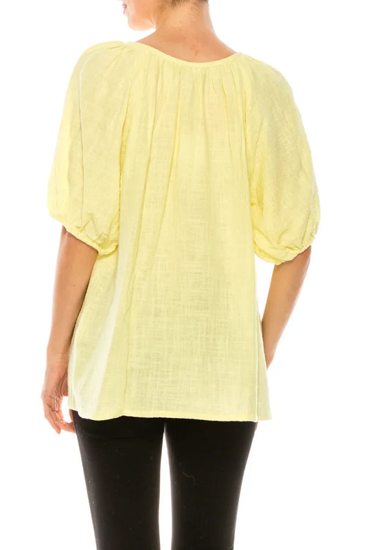 Back view of a woman wearing a pale yellow puff-sleeve blouse and black trousers.