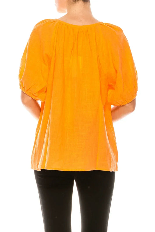 Rear view of a woman wearing a bright orange puff-sleeve linen blouse and black pants.