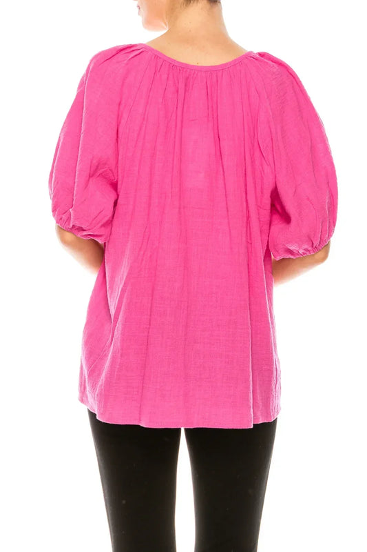 Back view of a woman wearing a bright pink puff sleeve blouse and black pants.
