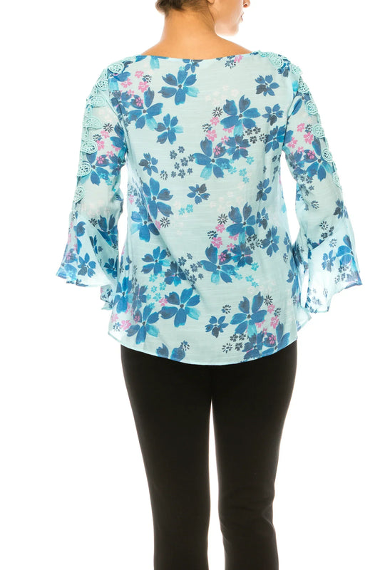 Back view of a woman wearing a light blue floral print blouse with bell sleeves and black pants.