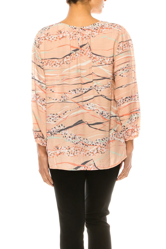 Back view of a woman wearing a peach patterned long-sleeve blouse and black pants.