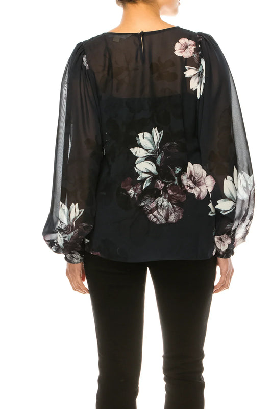 Back view of a woman wearing a black floral sheer blouse and black trousers.