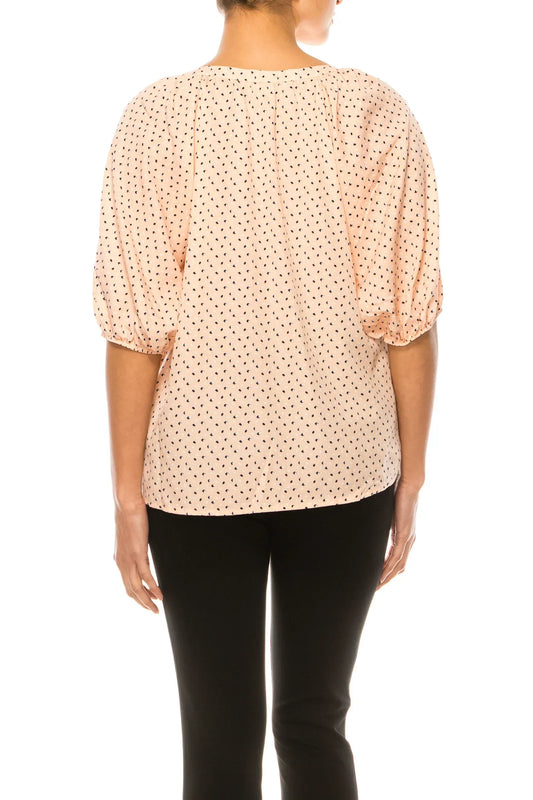 Back view of a woman wearing a peach dotted blouse with puff sleeves and black trousers.