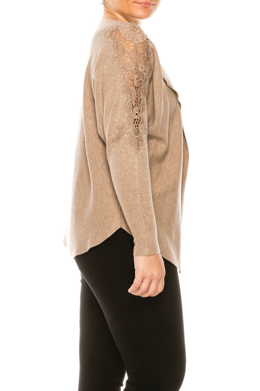 Woman wearing a beige knit cardigan with lace and rhinestone sleeve details and black pants.