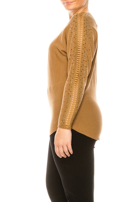 Woman wearing a tan long-sleeve sweater with decorative beaded and braided sleeve details.