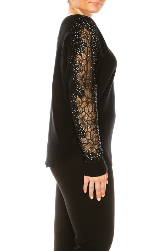 Woman wearing a black long-sleeve top with floral lace and rhinestone sleeve detail.