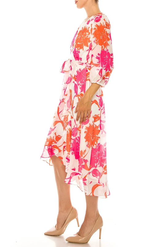 Woman wearing a white midi dress with vibrant pink and orange floral prints and nude heels.