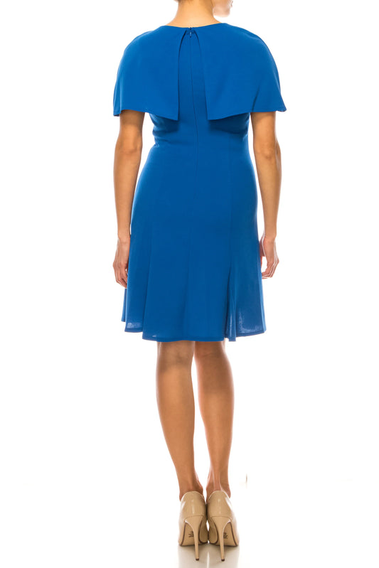 Back view of a woman wearing an elegant royal blue cape-style knee-length dress and nude heels.