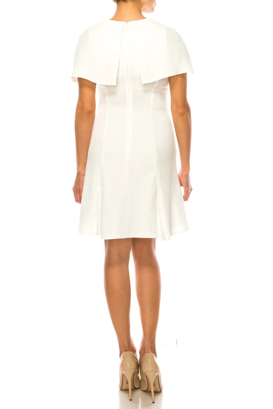 Back view of a woman wearing an elegant white knee-length dress with a capelet detail.