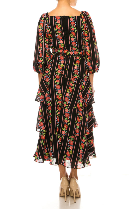 Back view of a woman wearing a black floral tiered maxi dress with long sleeves and a belt.