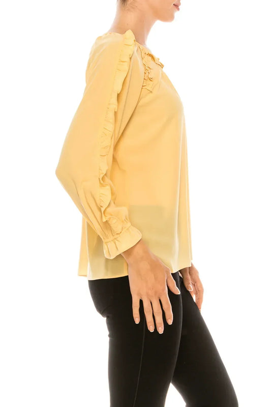 Woman wearing a yellow long-sleeve ruffle blouse and black pants.