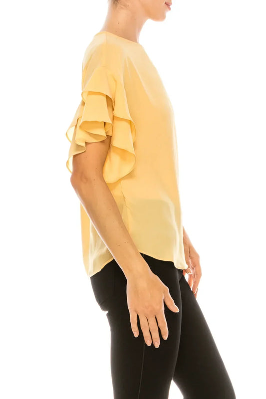 Woman wearing a pale yellow blouse with ruffle sleeves and black trousers.