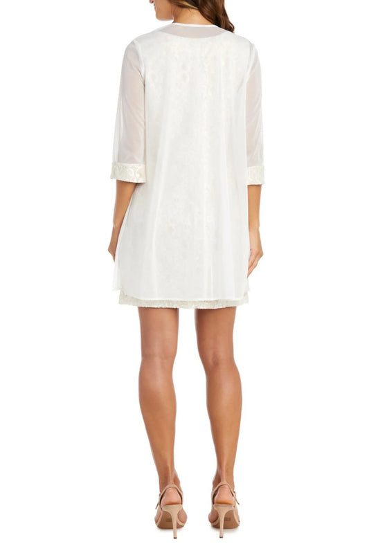 Back view of a woman wearing a white RM RICHARDS lace sheath dress with a matching jacket.
