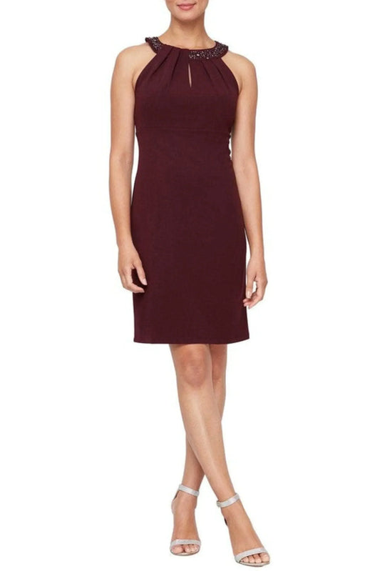 Woman wearing a burgundy sleeveless cocktail dress with embellished neckline and keyhole detail