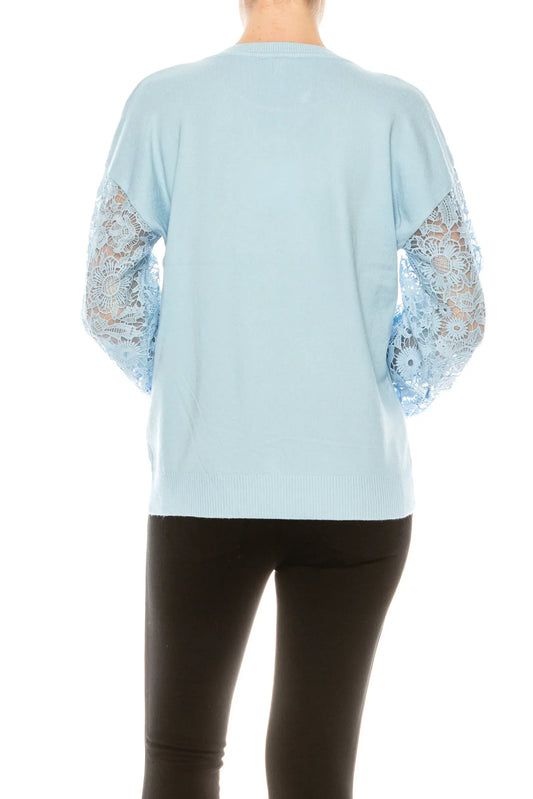 Back view of a woman wearing a light blue sweater with lace sleeves and black pants.