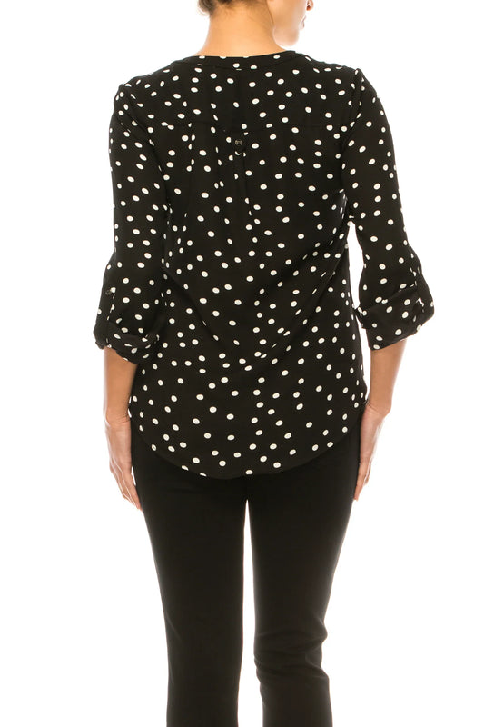 Rear view of a woman wearing a black and white polka dot blouse and black trousers.